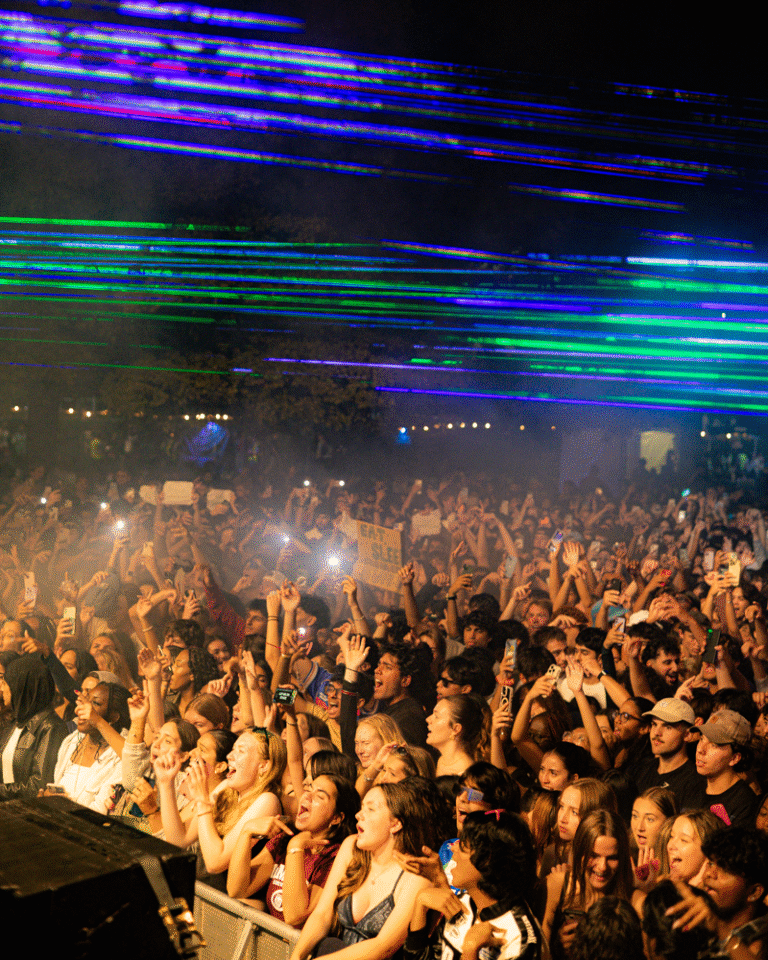Students singing and jumping at McMaster MSU concert with laser lights above.