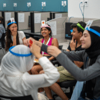 Students sitting in a circle playing a game called 'HEDBANZ'.