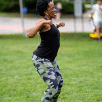 An instructor dancing on a field with a headset microphone.