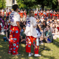 A large group of first-year students sitting on the grass listening to Faculty representatives who have a microphone.
