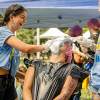 First-years putting a pie in a representative's face who is wearing a trash bag.