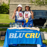 Faculty representatives standing behind a booth that reads ' MCMASTER SOCIAL SCIENCES BLU CRU'.