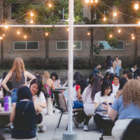 First-year students sitting at picnic tables, painting under string lights.