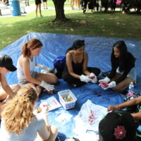 A group of first-year students and Faculty representatives sitting on a tarp, tie-dyeing T-shirts.