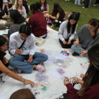 First-year students sitting on a tarp making bracelets.