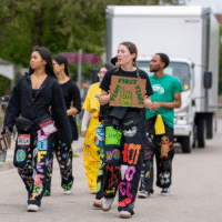 Faculty representatives walking on a road holding signs that say ' MAC SCI' and 'TEAM FIRST YEARS 28'.