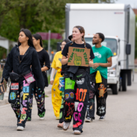 Faculty representatives walking on a road holding signs that say ' MAC SCI' and 'TEAM FIRST YEARS 28'.